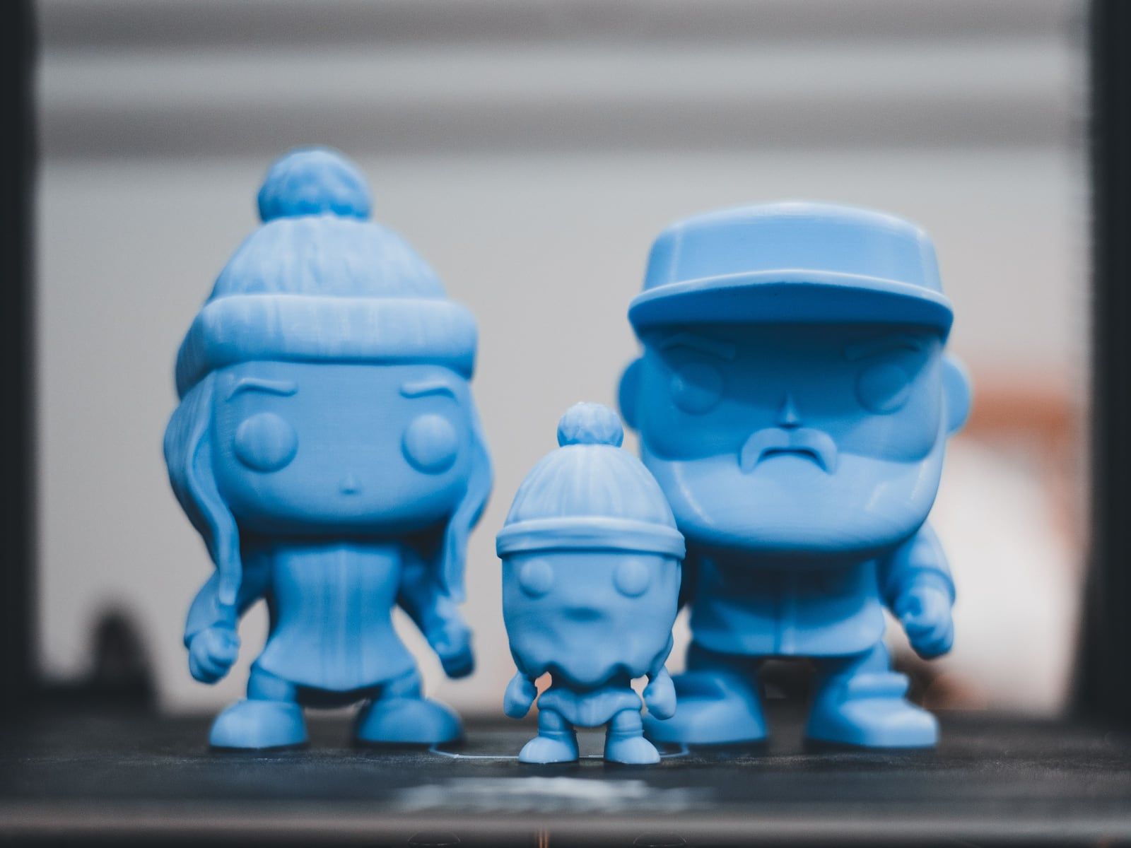 Drie blauwe 3D-geprinte figuurtjes met mutsen en een pet