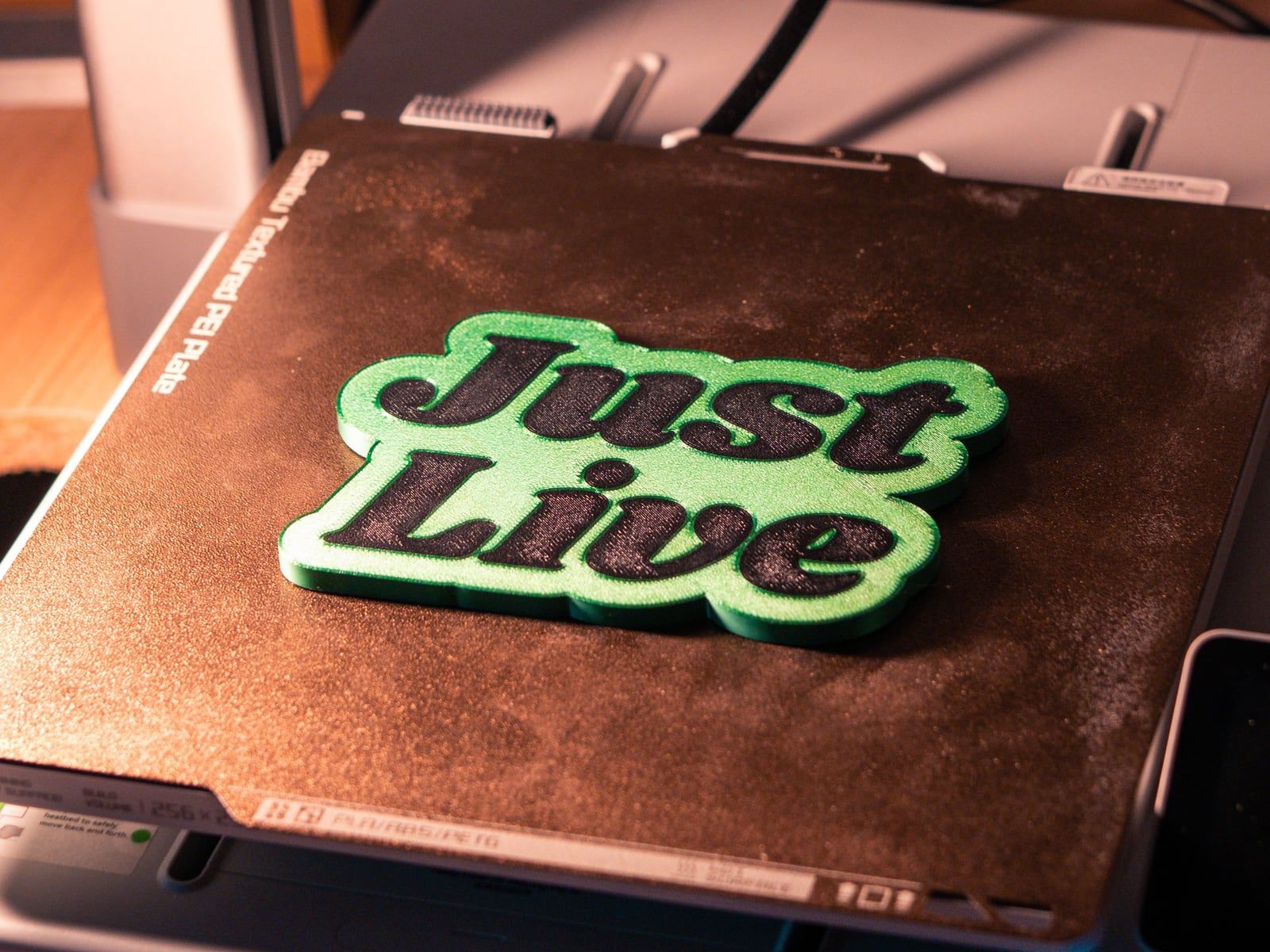 Een groen-zwart 3D-geprint embleem met tekst op het printbed