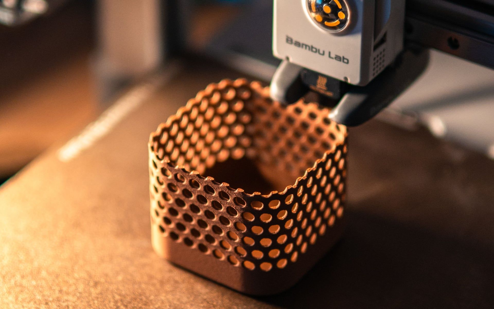Een 3D-printer die een koperkleurig bakje met open honingraatstructuur print