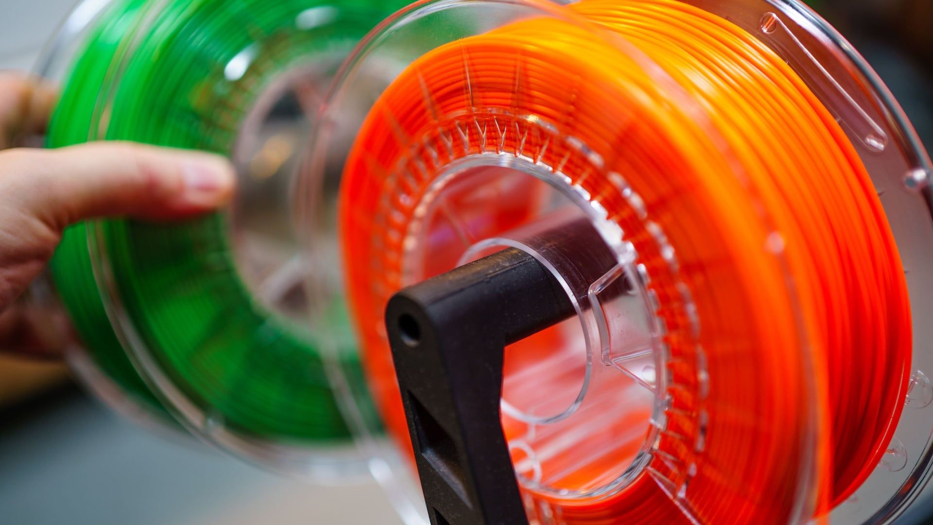 Twee rollen filament in fel oranje en groen op een spoelhouder