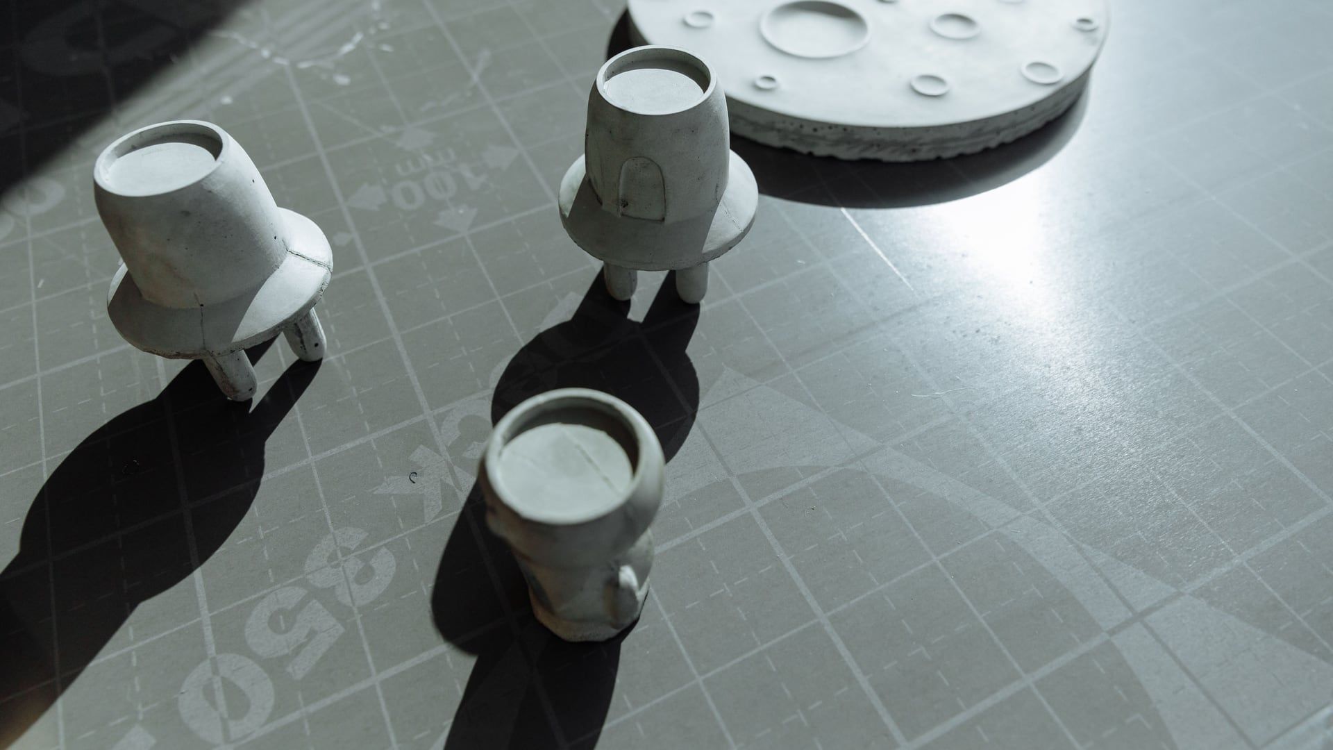 Grijze 3D-geprinte bekers en een maanvormige schijf op een snijmat