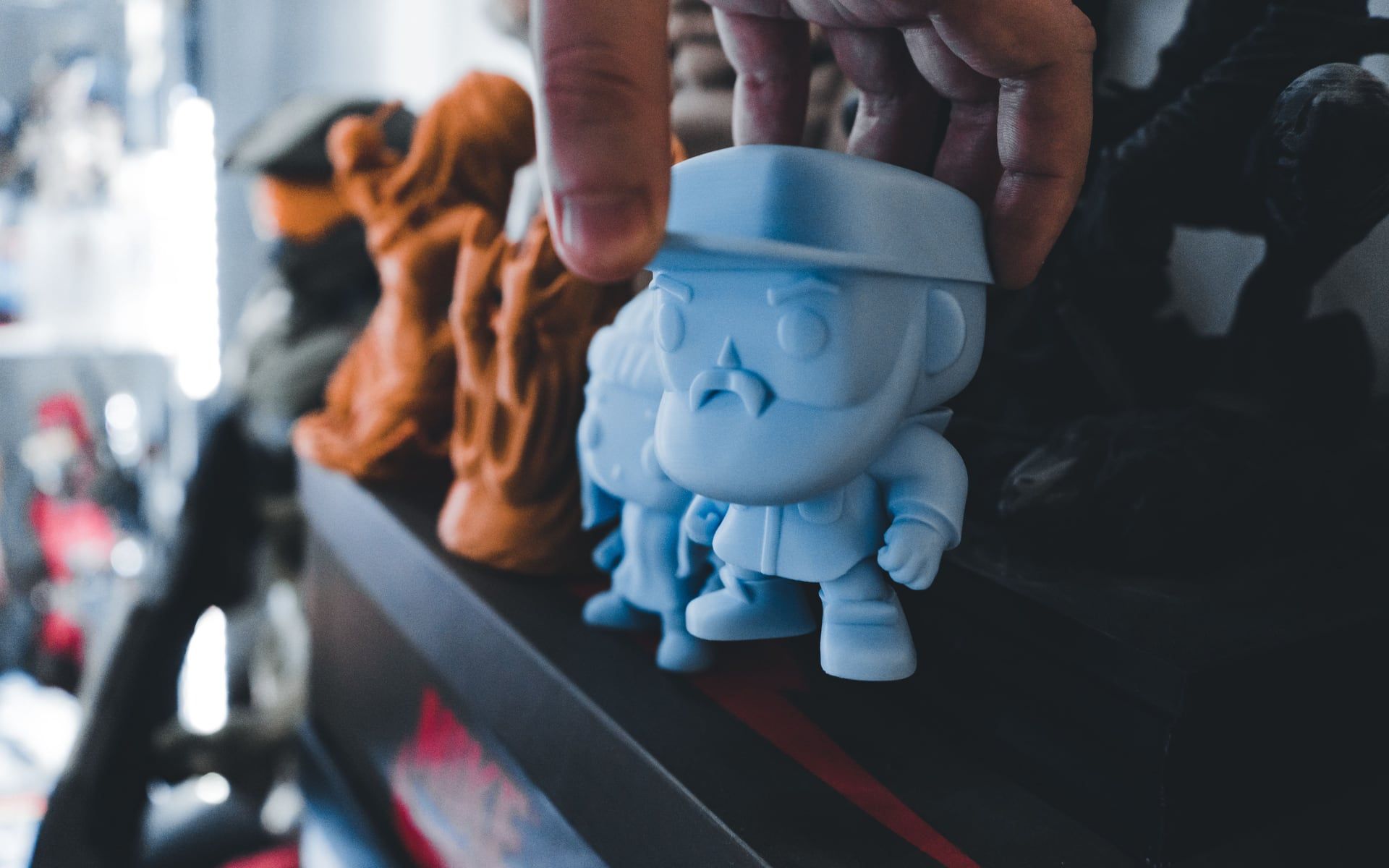 Een hand zet een blauw 3D-geprint figuurtje op een plank tussen andere prints